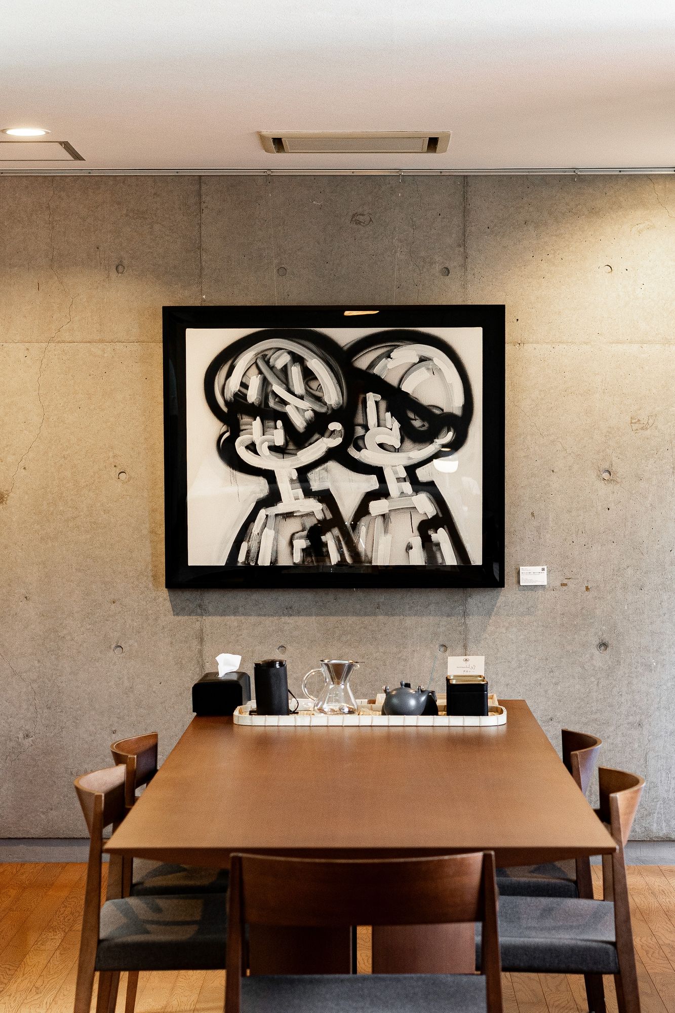 Timber dining table beneath a large black and white framed drawing on a concrete wall