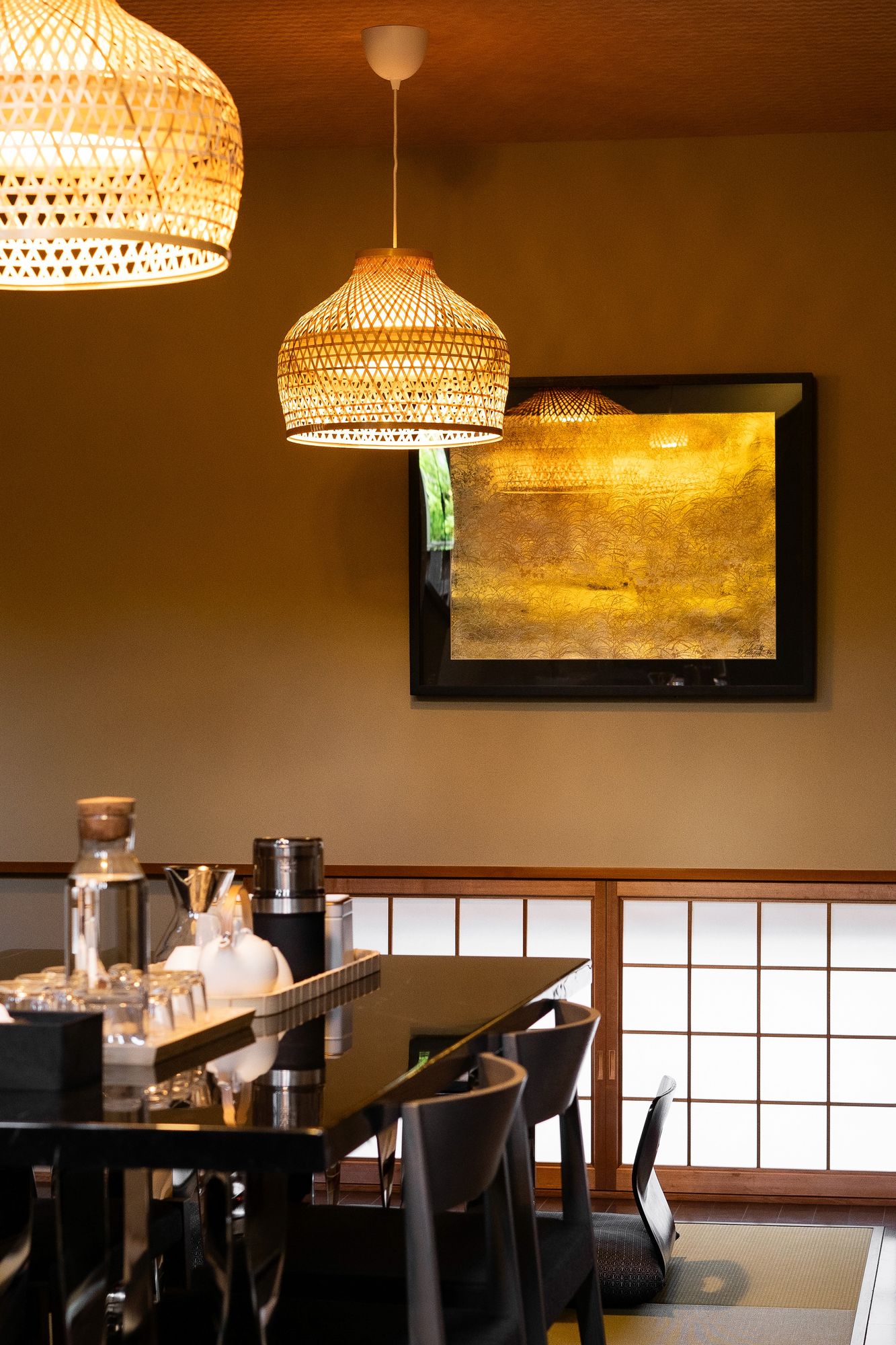 Dining table beneath woven pendants and a gold artwork