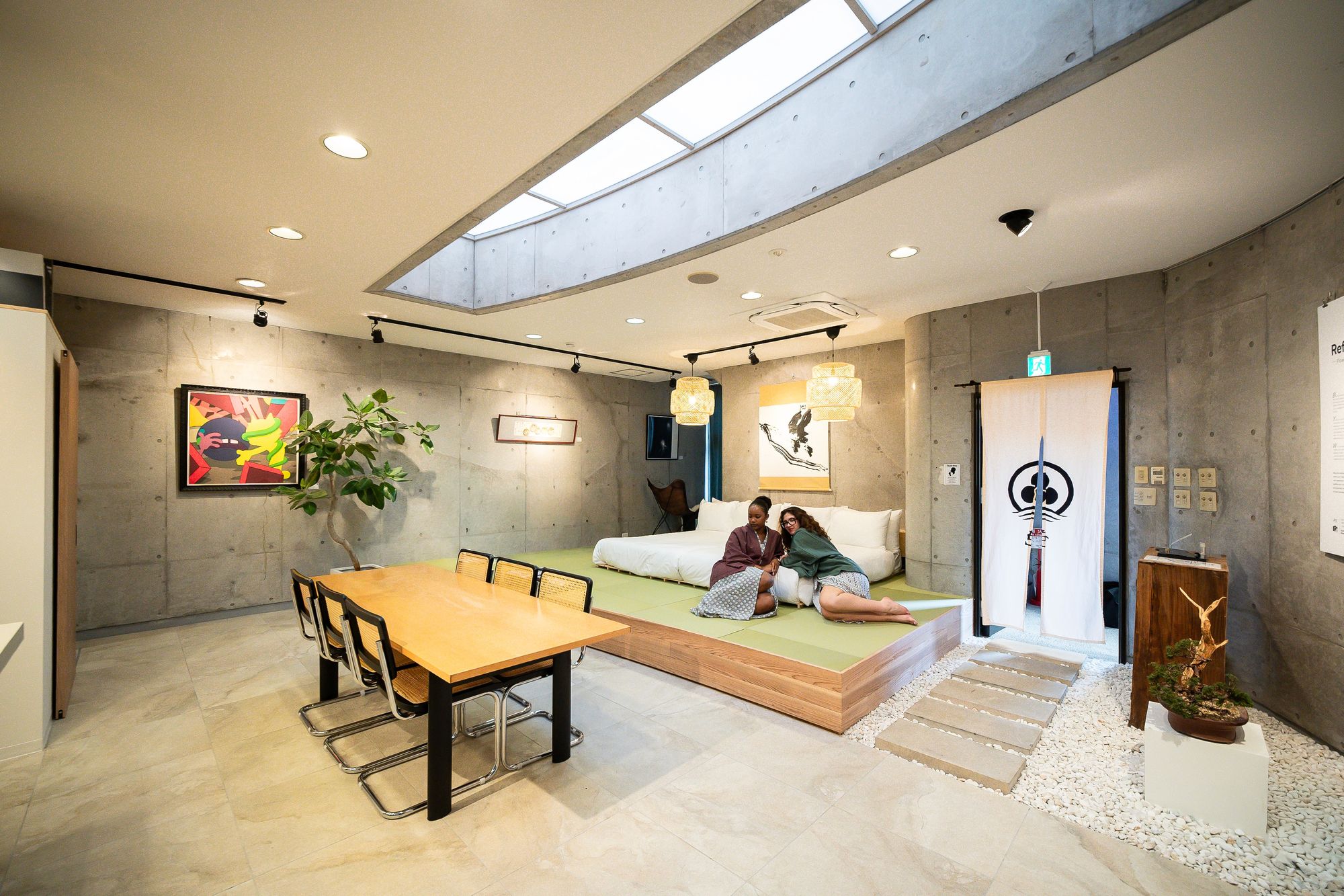 Guest room with curved concrete ceiling, long timber table and a raised tatami platform
