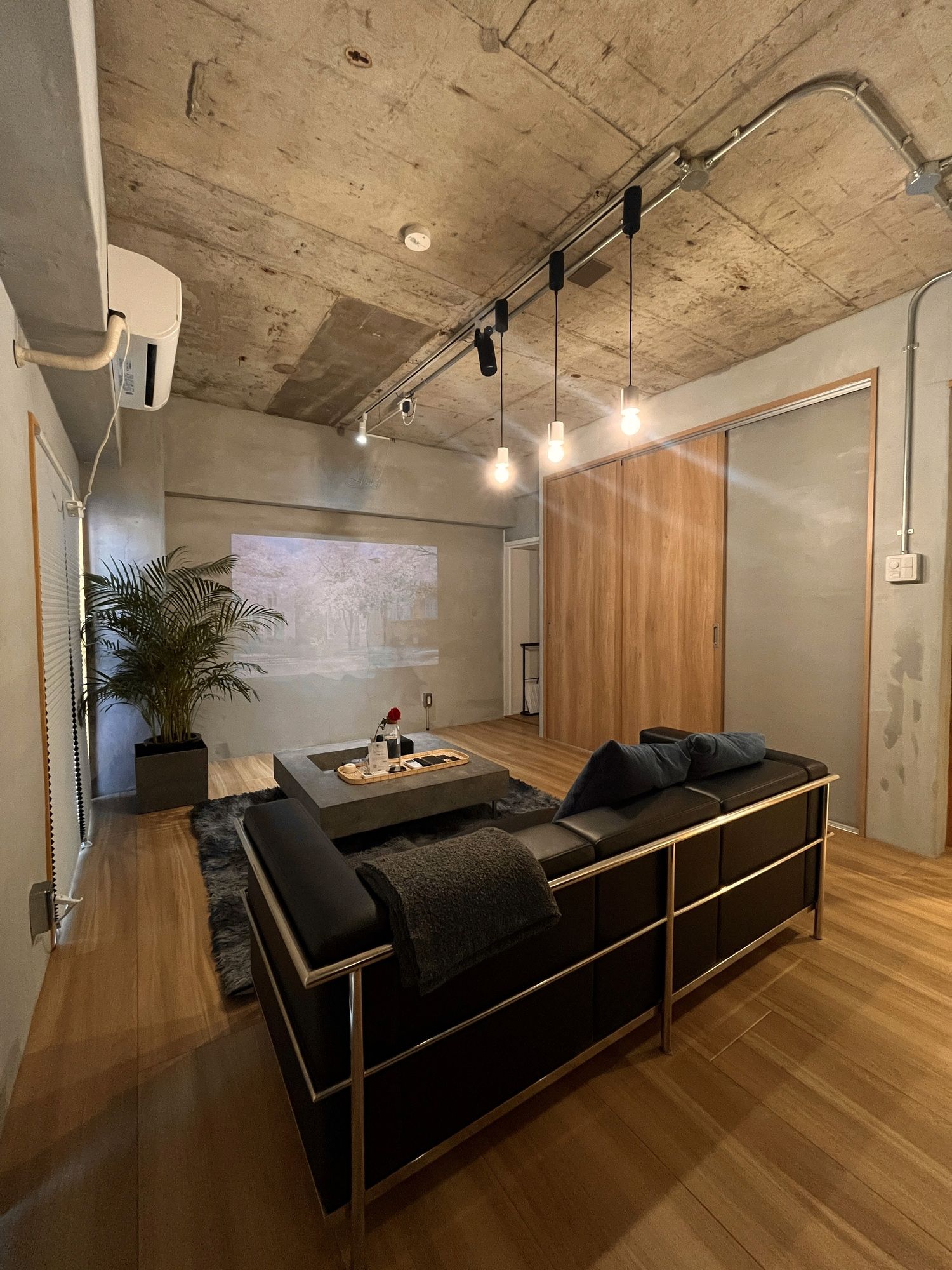 Bare concrete ceiling, timber wall and black leather seating on an oak floor