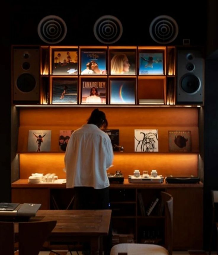 Guest choosing a record at a lit vinyl shelf with speakers above