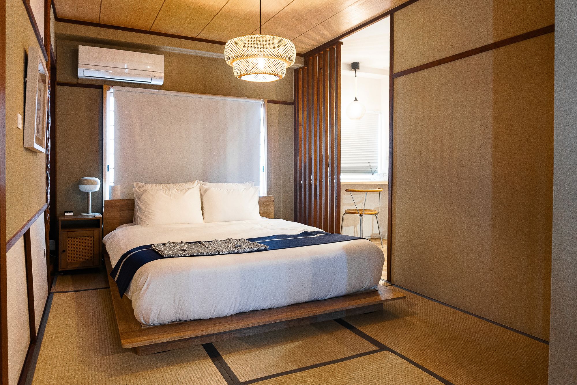 Issen - framed artwork above a bed dressed with a dark blue runner, under a pendant lamp in a wood and tatami room